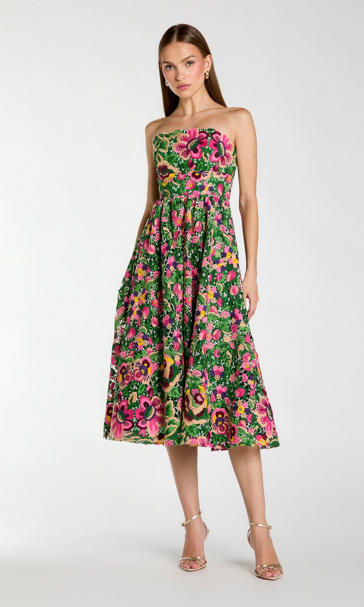 A woman wearing the Mac Duggal 56265 Midi Party Dress in Green Multi, featuring a strapless silhouette and vibrant pink, yellow, and red floral accents, stands in neutral heels against a plain light background.